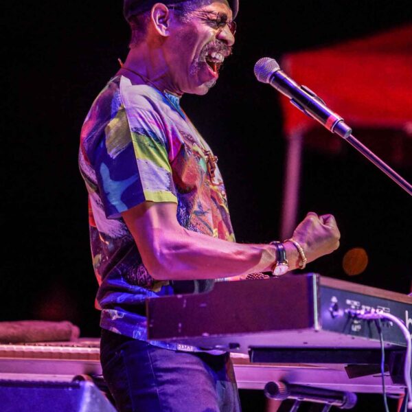 Lonnie Jordan on stage at the keyboard, singing into microphone with eyes closed and fist raised