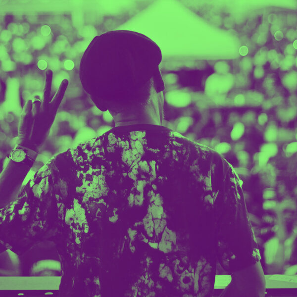 Duotone photo from behind of War the band's Lonnie Jordan, on stage giving a live outdoor festival audience a peace sign salute.