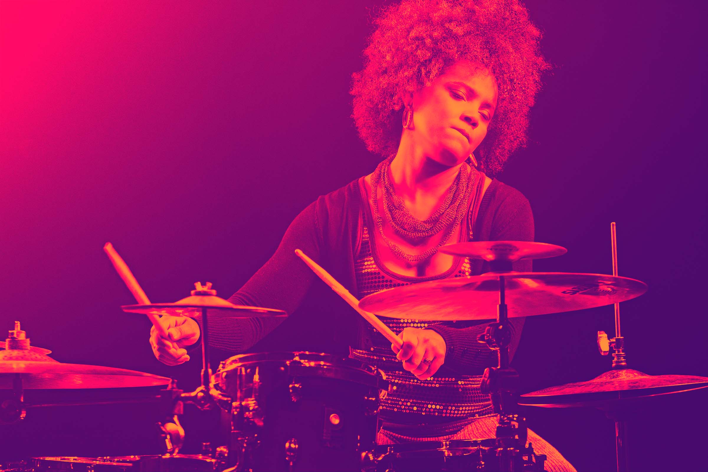 A large duotone photo of Yissy Garcia, eyes closed, playing the drums live.